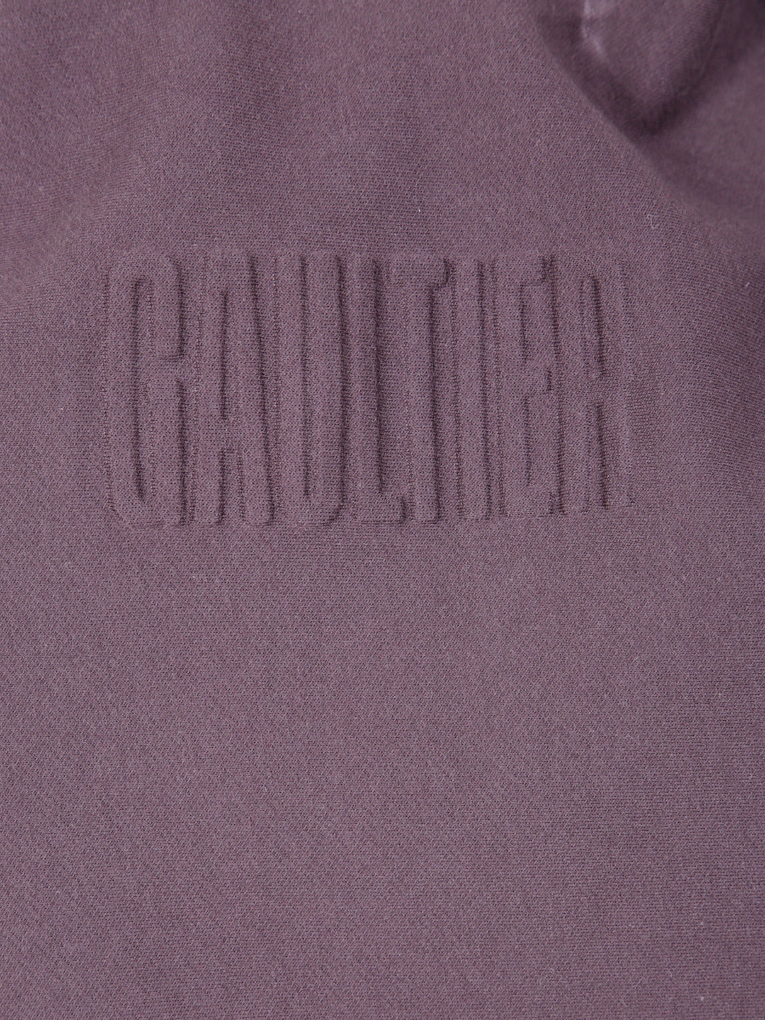 Close-up of a textured fabric with 'Gaultier' branding on a purple background