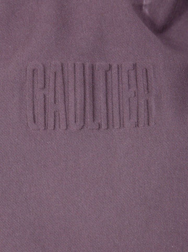 Close-up of a textured fabric with 'Gaultier' branding on a purple background