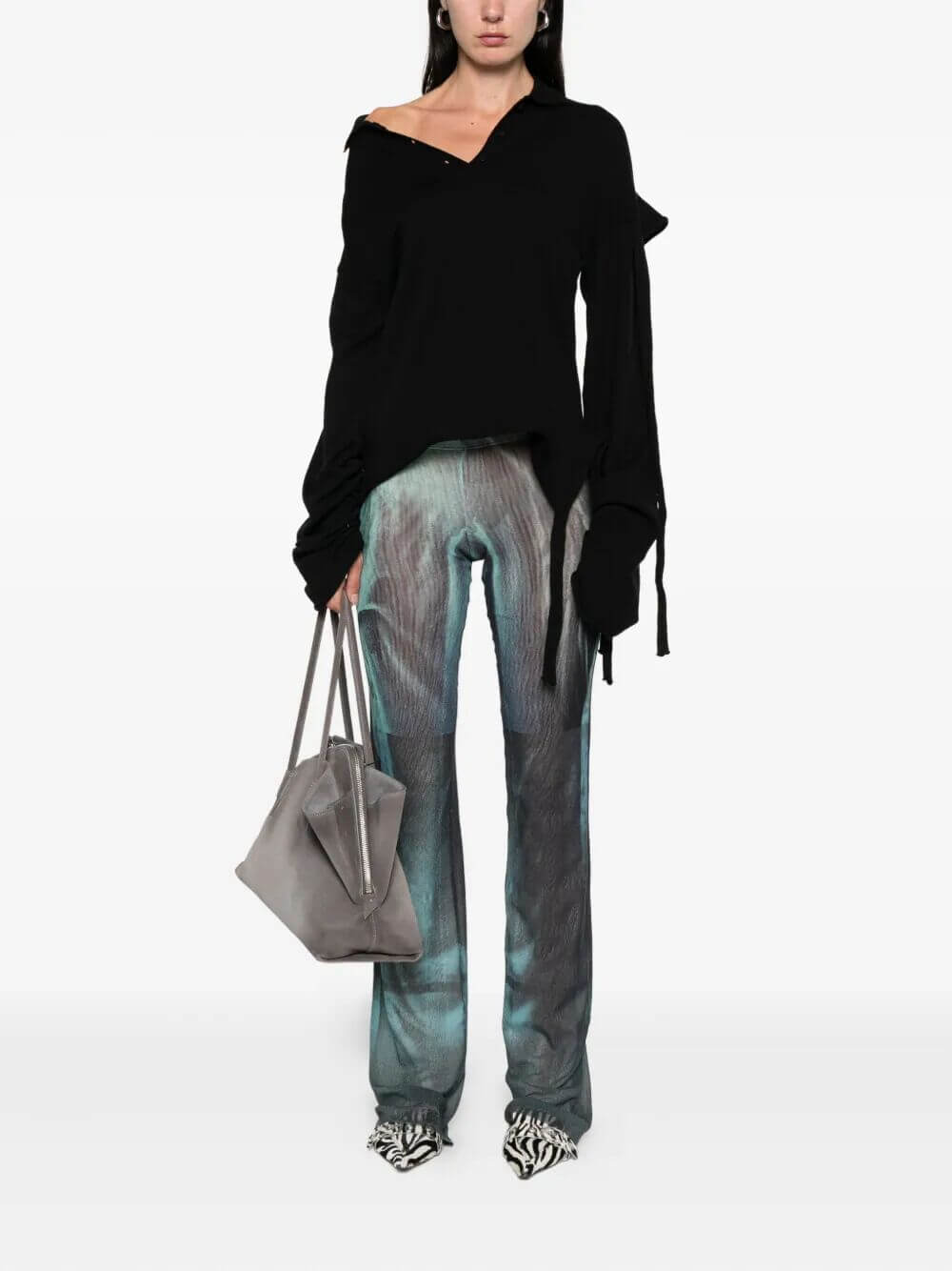 Person wearing a black sweater and tie-dye pants holding a gray bag on a white background