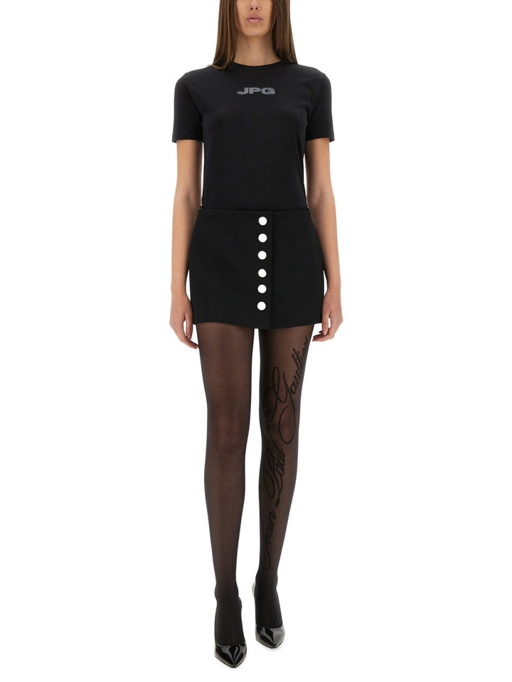 Person wearing a black t-shirt with 'JPG' logo, black skirt with buttons, and black stockings on a white background