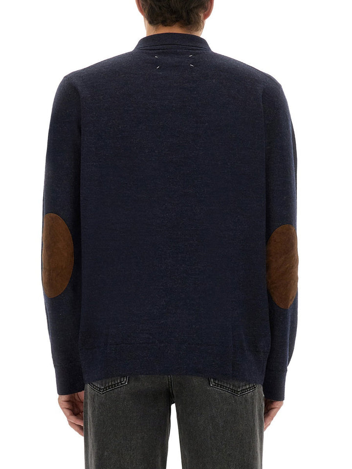 Navy sweater with brown elbow patches worn by a person on a white background