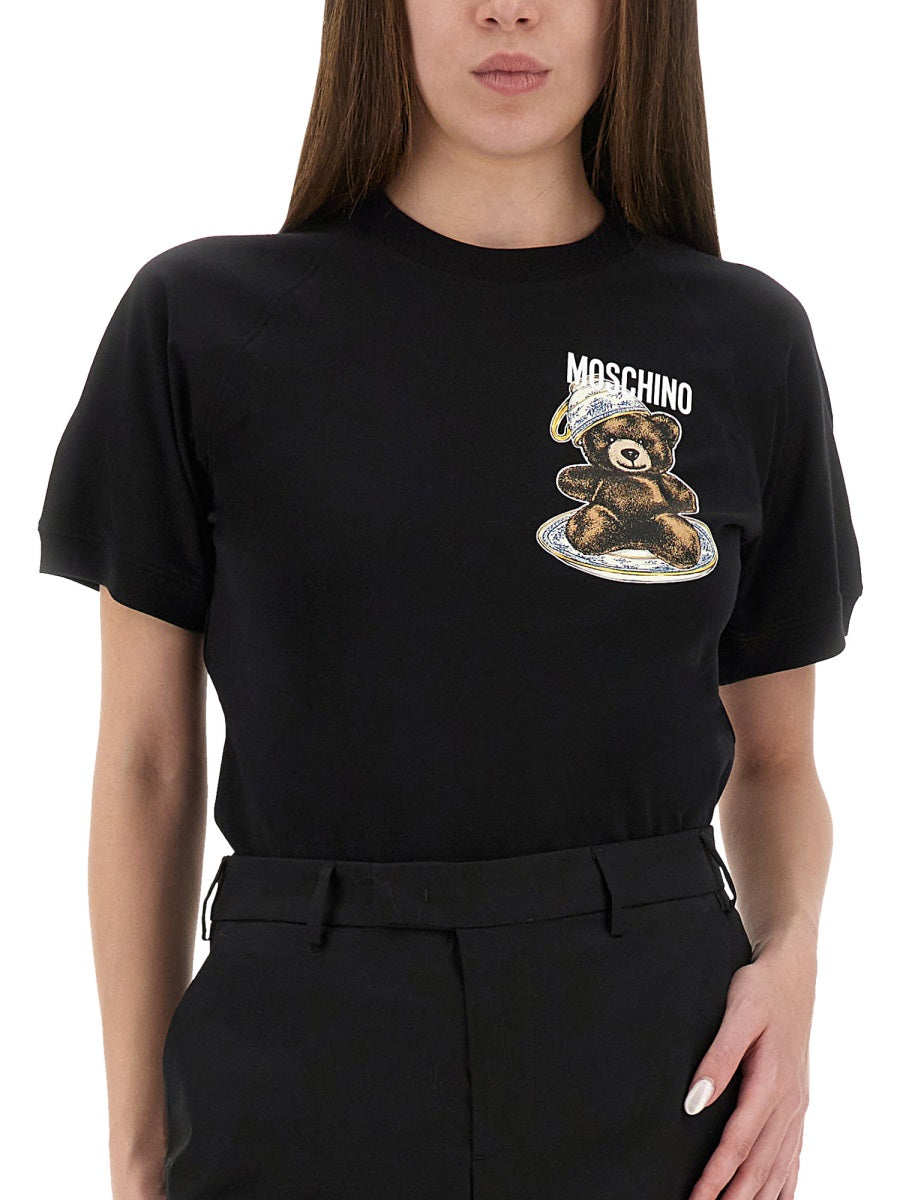 Person wearing a black t-shirt with a bear graphic and 'Moschino' logo.
