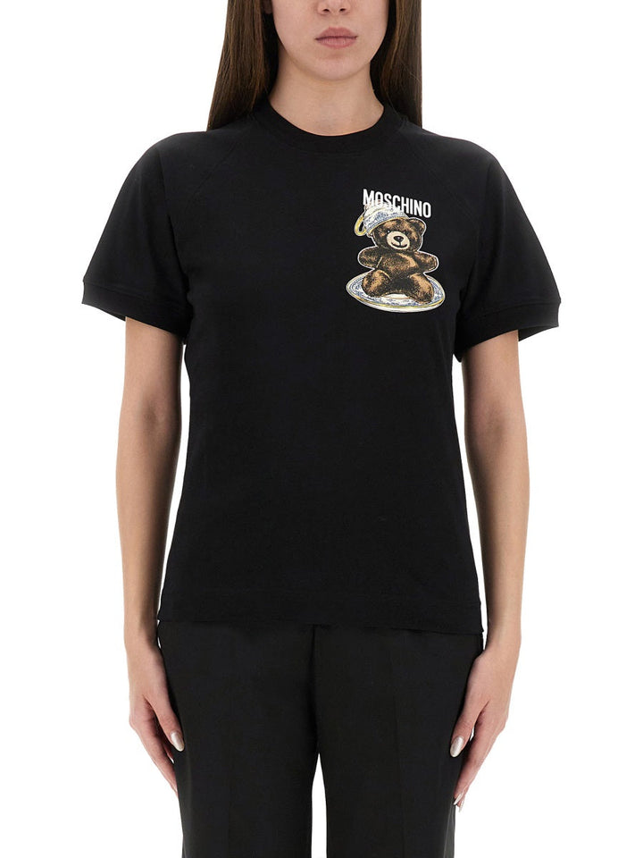 Person wearing a black t-shirt with a teddy bear graphic and 'Moschino' branding.