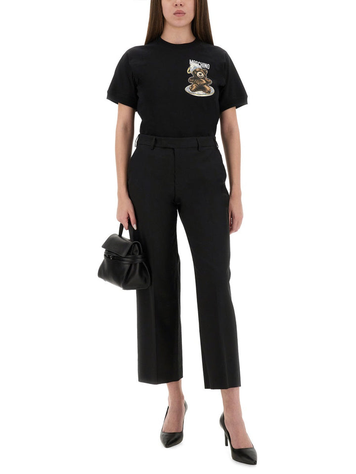 Woman wearing a black t-shirt with a graphic design and black pants, holding a black handbag on a white background.