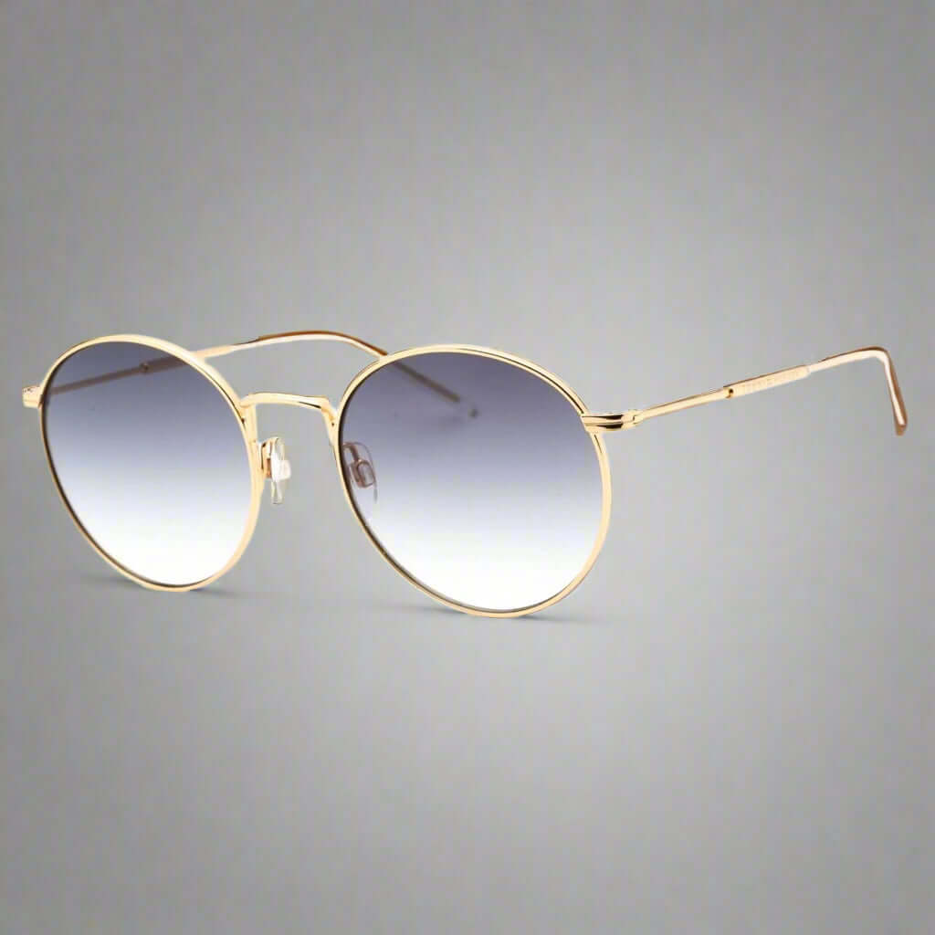 Round sunglasses with gold frame and gradient blue lenses on a white background