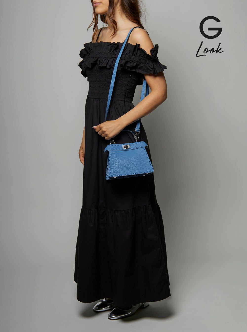 Woman in a black dress holding a blue handbag against a gray background, with 'G Look' branding.