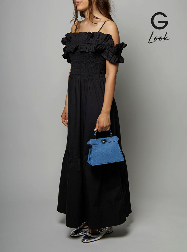 Woman wearing a black off-shoulder dress holding a blue handbag on a gray background