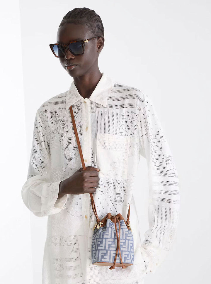 Person wearing a white lace outfit holding a patterned handbag against a white background