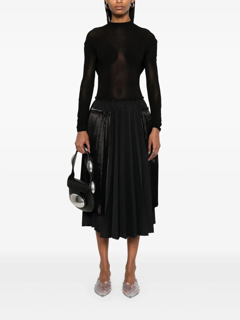 Person wearing a black long-sleeve top and black skirt holding a black handbag on a white background