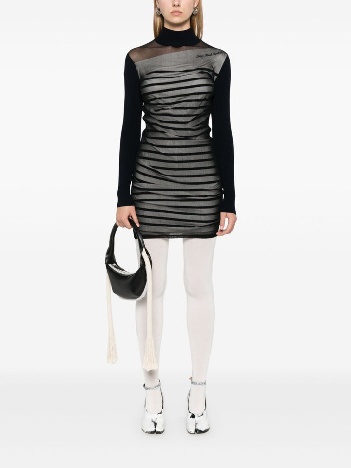 Person wearing a black and gray dress with sheer panels on a white background