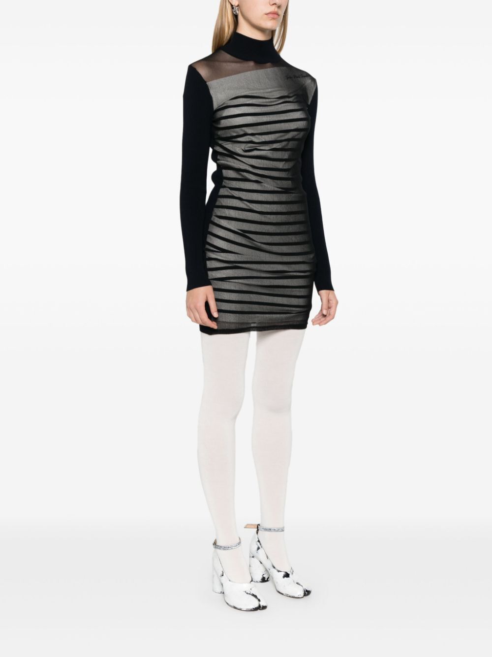 Person wearing a black and gray dress with white tights on a white background