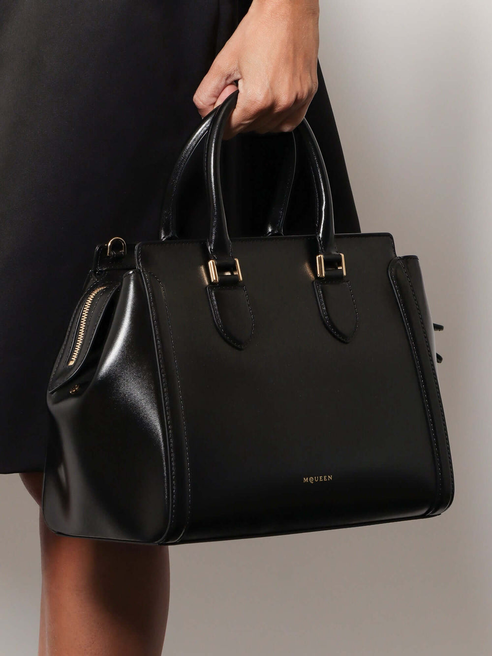 Black handbag held by a person against a neutral background