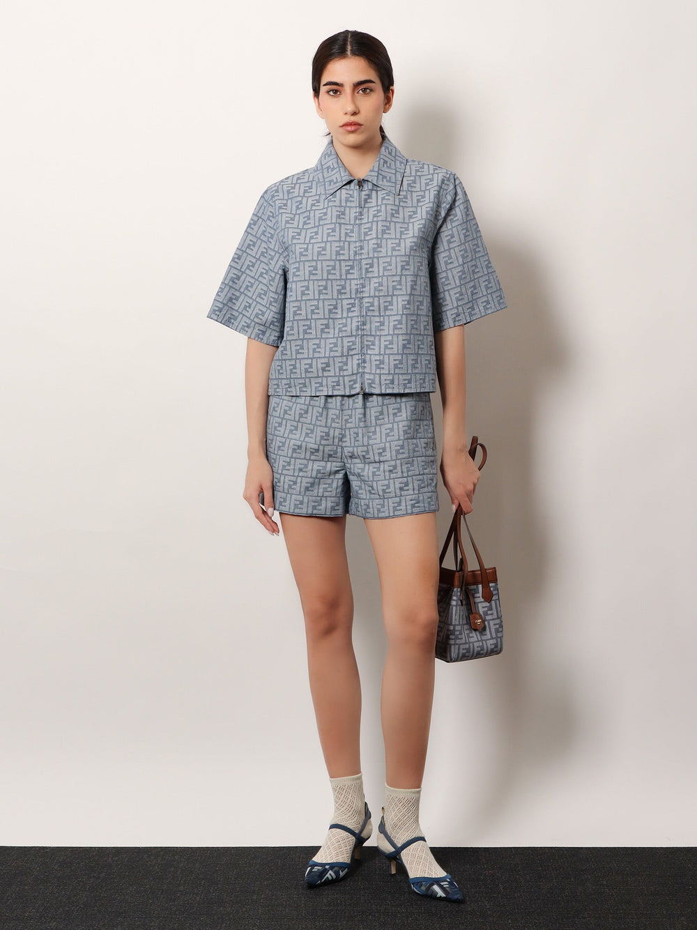 Woman wearing a matching blue and white patterned shirt and shorts set, holding a handbag.