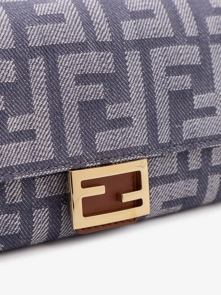 Close-up of a blue patterned handbag with a gold and brown logo plaque.
