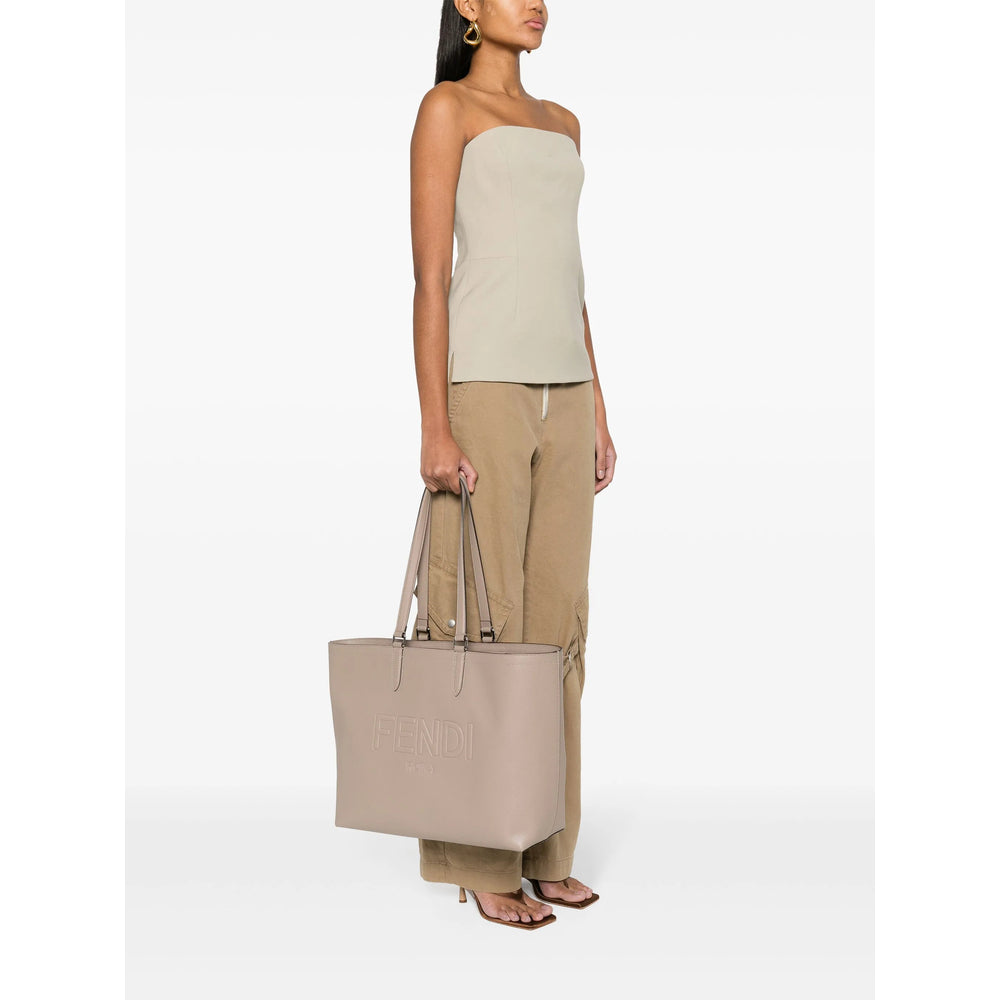 Woman holding a beige tote bag against a white background