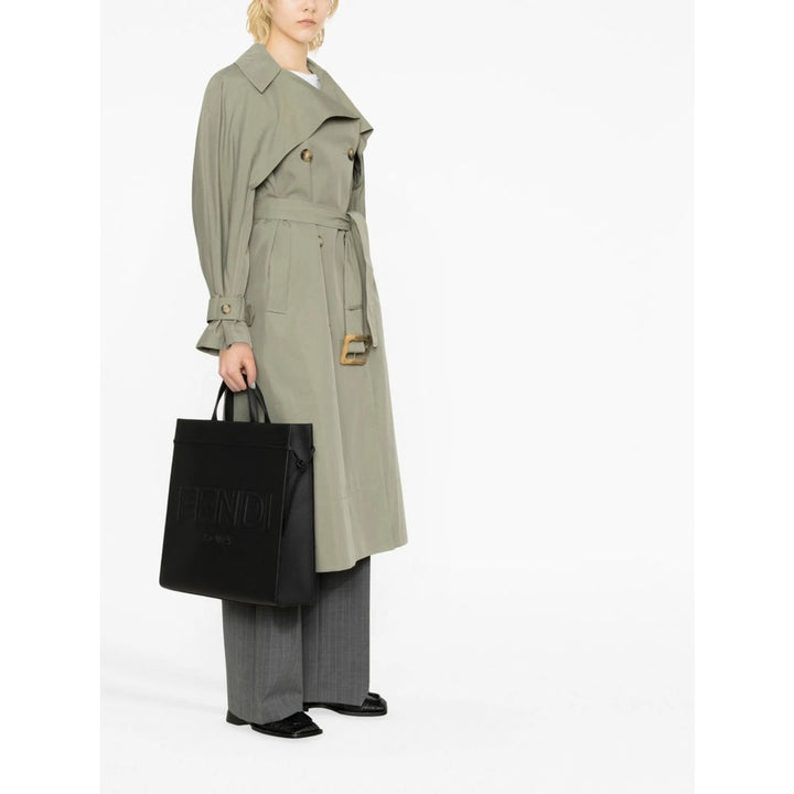 Person wearing a green trench coat holding a black bag on a white background