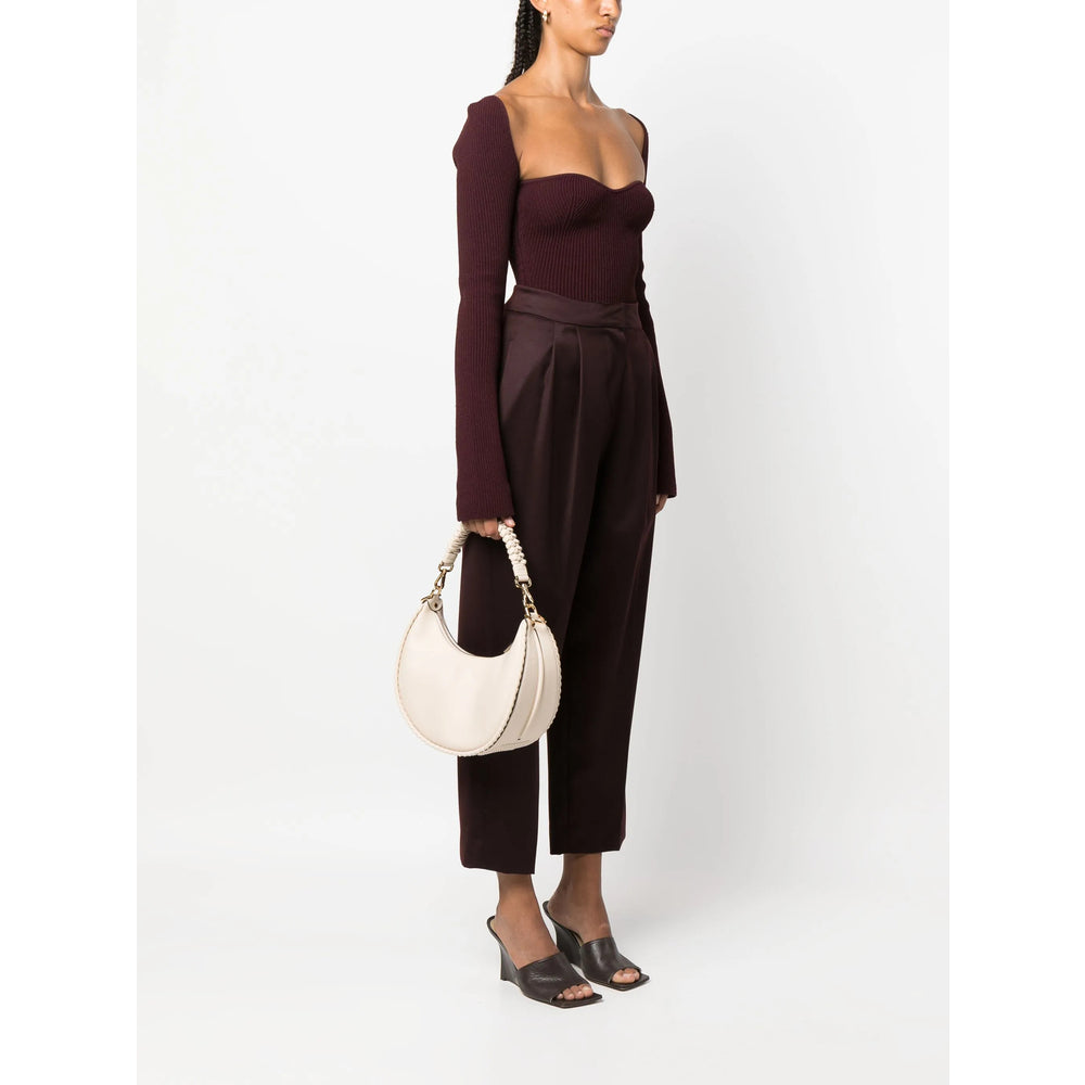 Woman wearing a dark brown outfit holding a white handbag on a white background