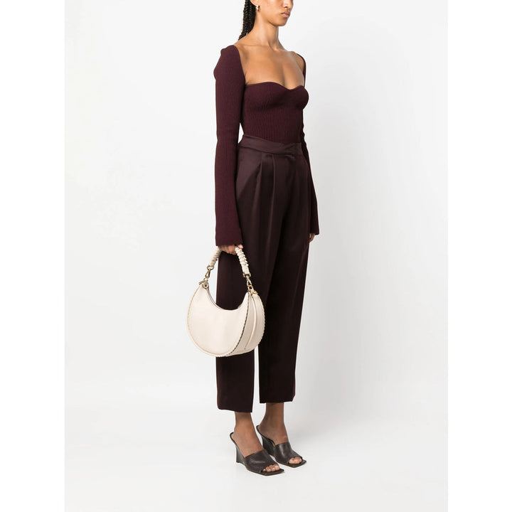 Woman wearing a dark brown outfit holding a white handbag on a white background