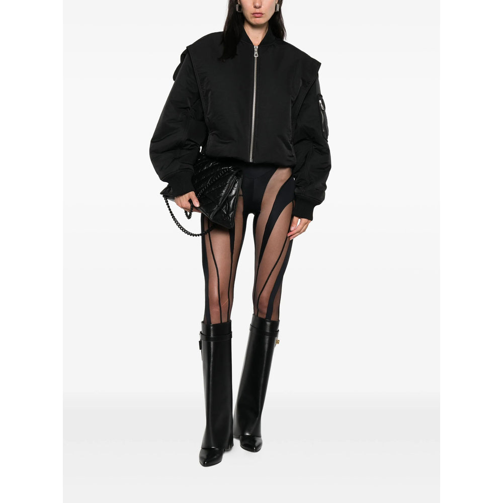 Person wearing a black bomber jacket, sheer black stockings, and black boots on a white background