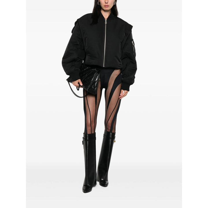 Person wearing a black bomber jacket, sheer black stockings, and black boots on a white background