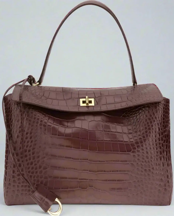 Brown crocodile-patterned handbag with a gold clasp on a white background