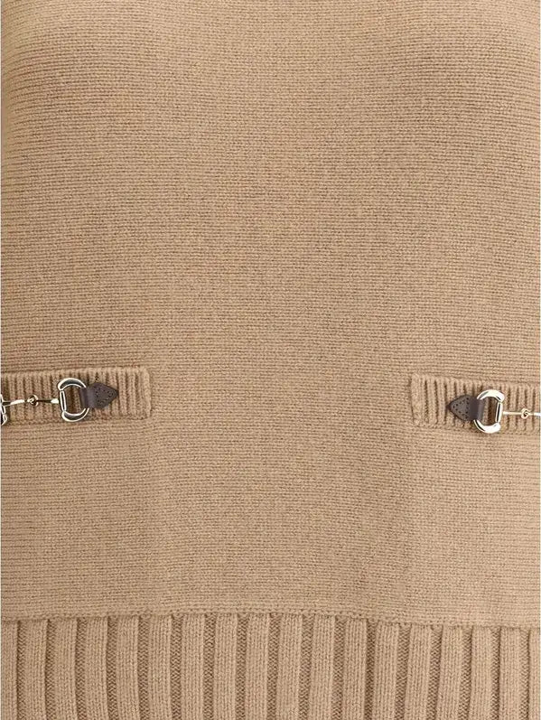 Close-up of a beige knitted sweater with ribbed hem and metal buttons.