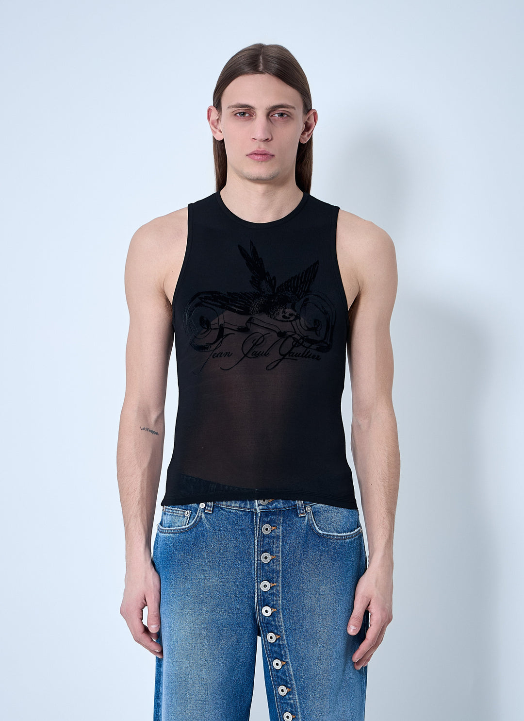 Person wearing a black sleeveless top with text and blue jeans on a light gray background