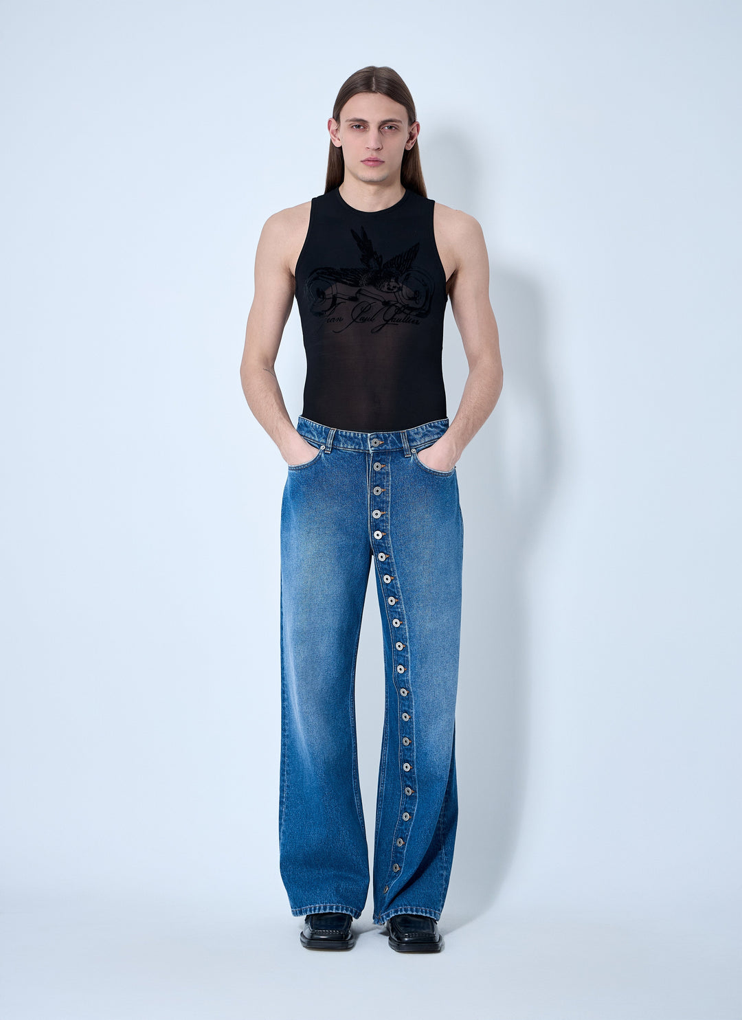 Person wearing a black sleeveless top and blue jeans with button details on a white background