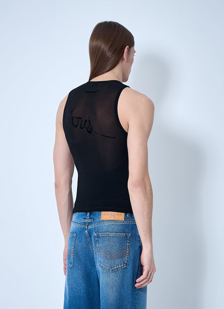 Woman wearing a black sleeveless top with sheer back panels and blue jeans on a light gray background