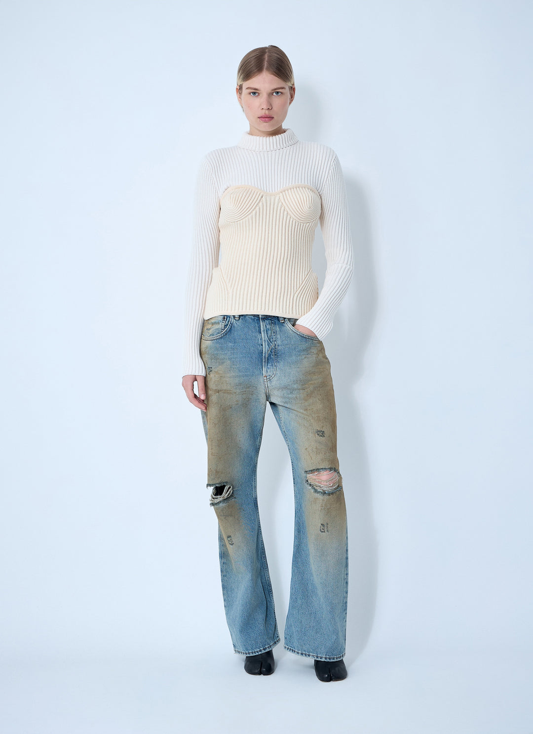 Person wearing a cream sweater and blue jeans with a white background