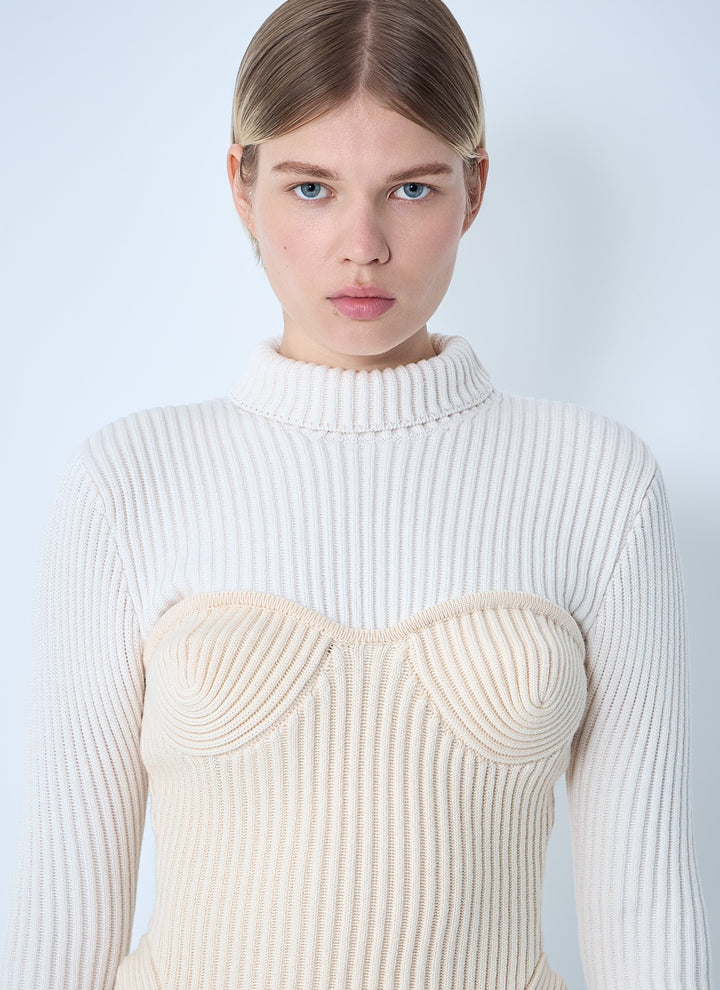 Woman wearing a cream ribbed sweater against a light blue background