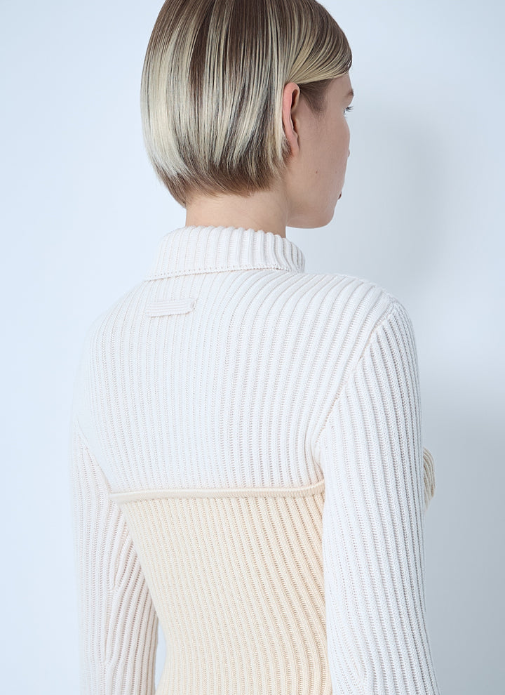 Person wearing a white ribbed sweater with a visible brand logo on a light gray background