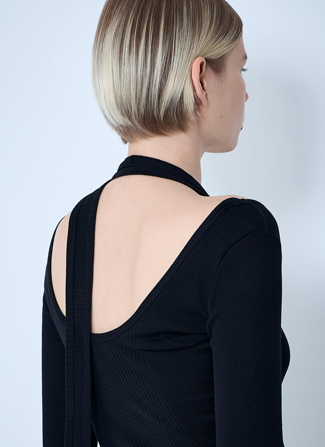Person wearing a black dress with a cut-out back against a light gray background