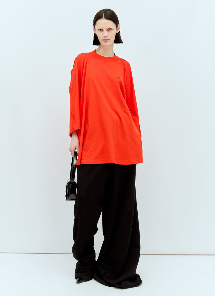 Person wearing a bright orange top and black pants on a white background