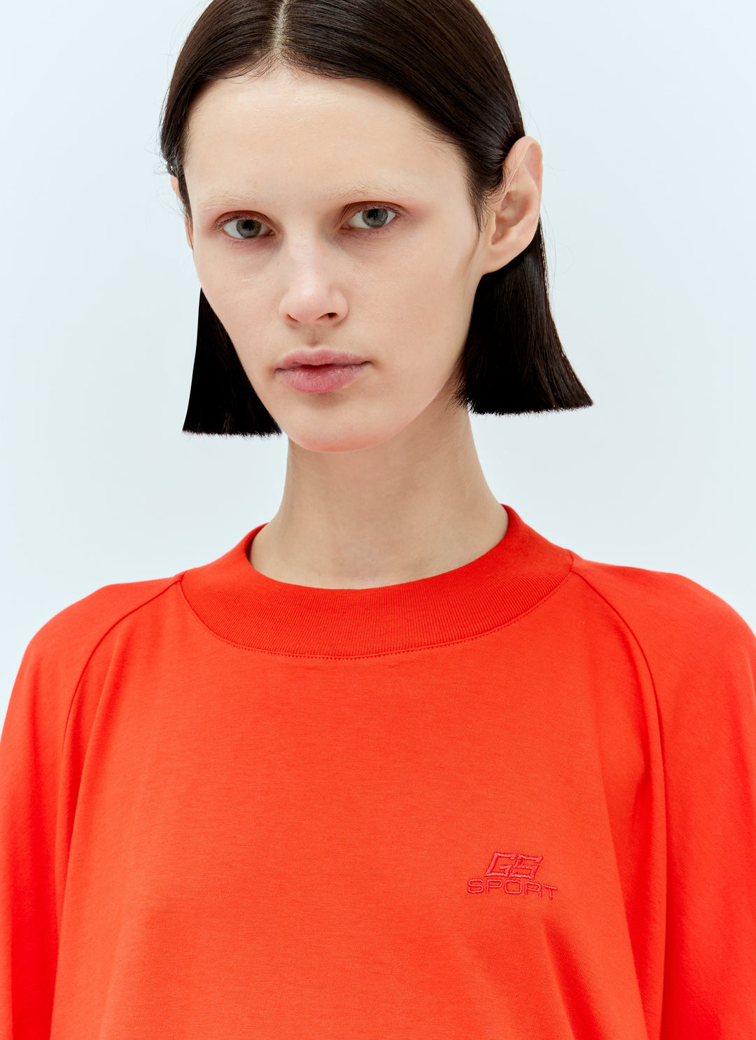 Person wearing a bright orange sweatshirt with a logo on a light gray background