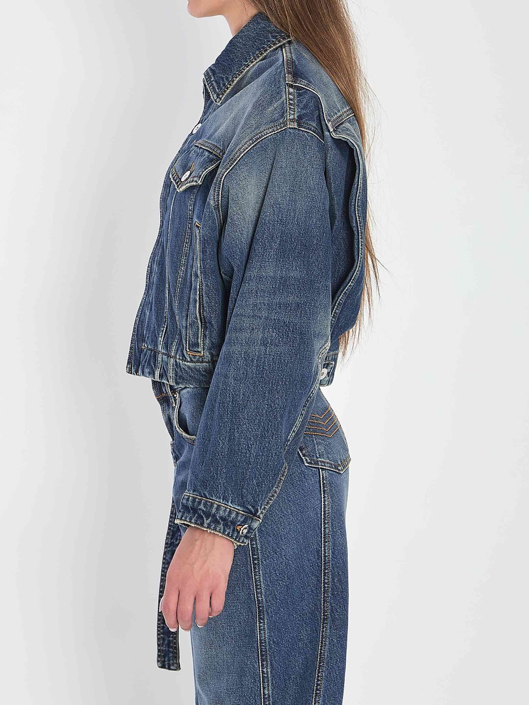 Person wearing a blue denim jacket and jeans on a white background