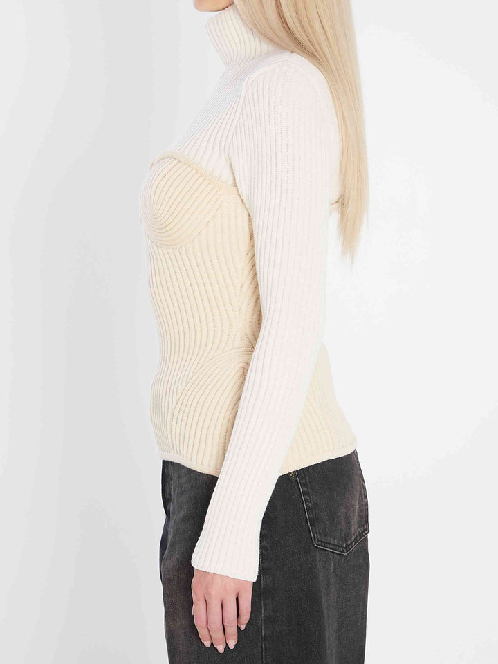 Person wearing a cream ribbed sweater and dark jeans on a white background