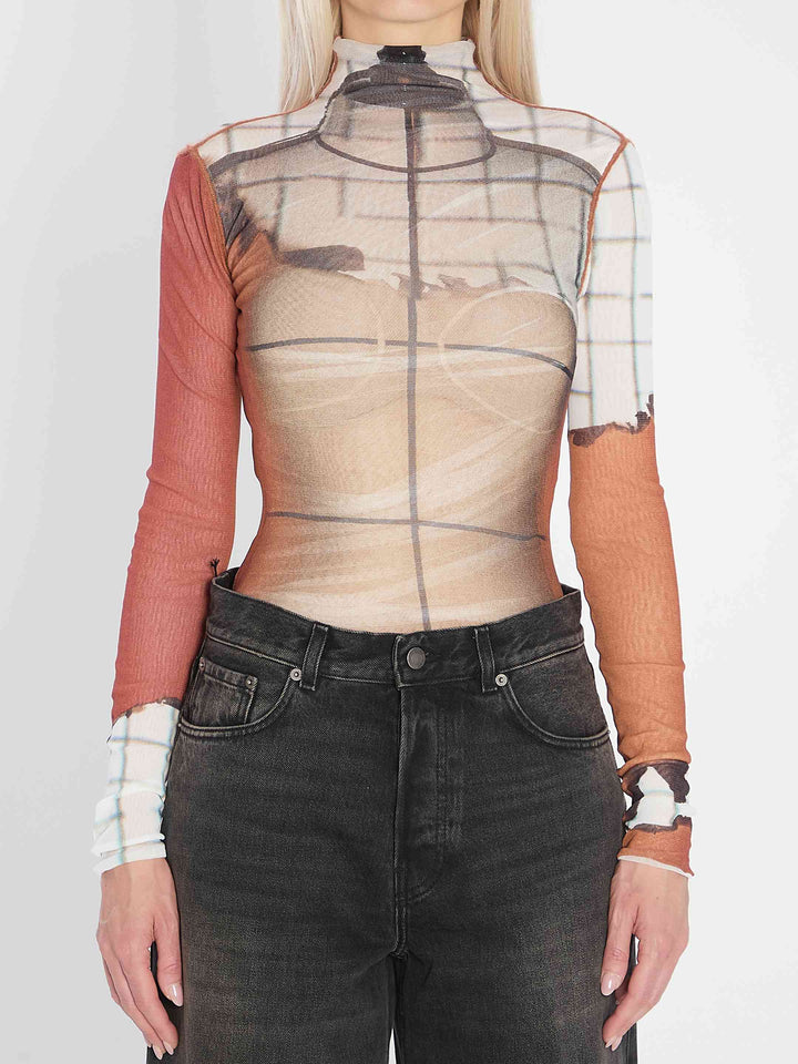 Person wearing a sheer top with long sleeves and dark jeans on a white background