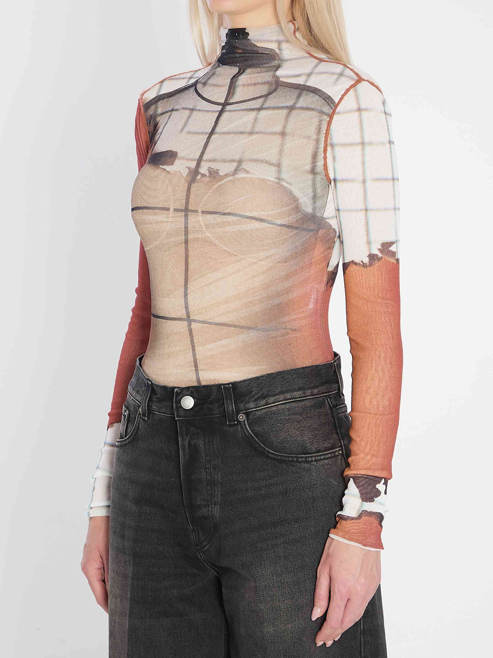 Person wearing a sheer top with geometric patterns and dark jeans on a white background