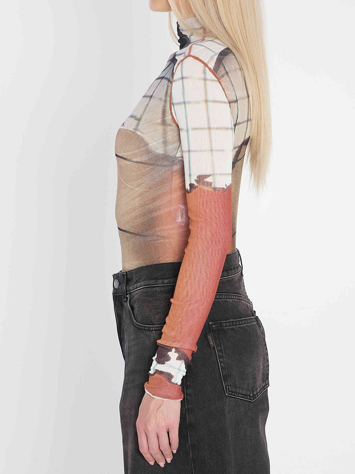 Person wearing a plaid shirt with sheer sleeves over a long-sleeve shirt, paired with dark jeans on a white background.