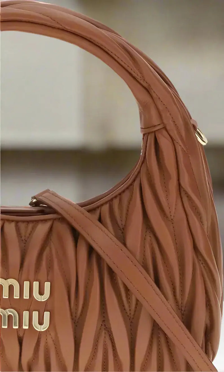 Brown handbag with quilted design and visible 'miu miu' logo on a white background