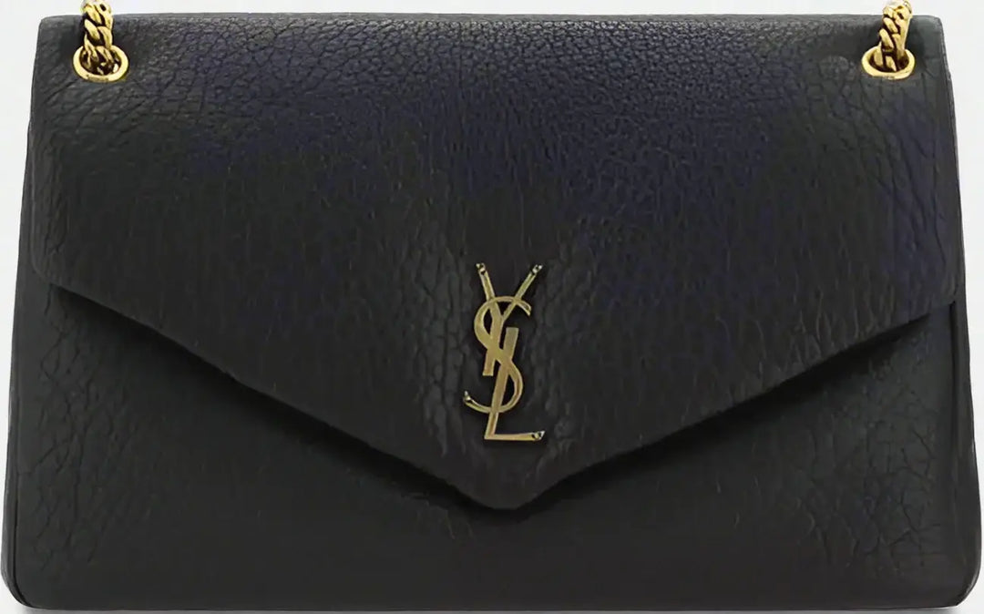 Black leather handbag with gold chain and logo on a black background