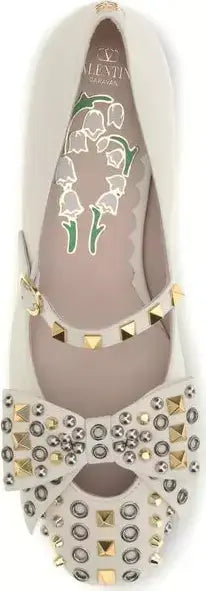 White flat shoe with gold studs and floral design on a white background