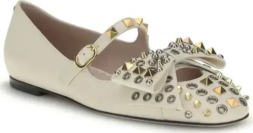 Beige flat shoe with gold and silver studded details on a white background