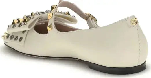 White flat shoe with gold studs on a white background