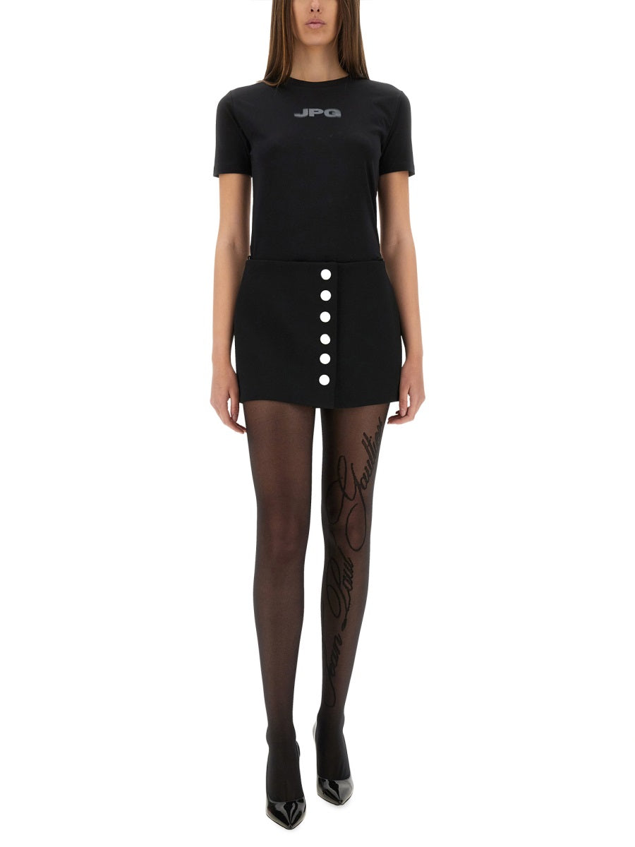 Person wearing a black t-shirt with 'JPG' logo, black skirt with buttons, and black stockings on a white background