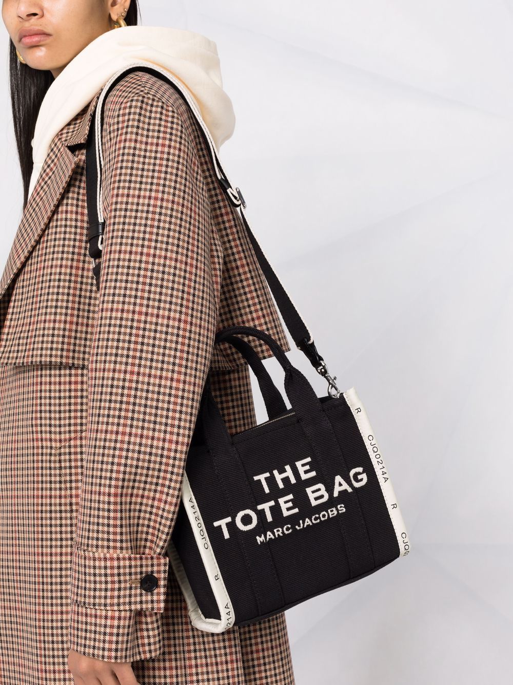 Person wearing a plaid coat holding a black tote bag with 'Marc Jacobs' branding.