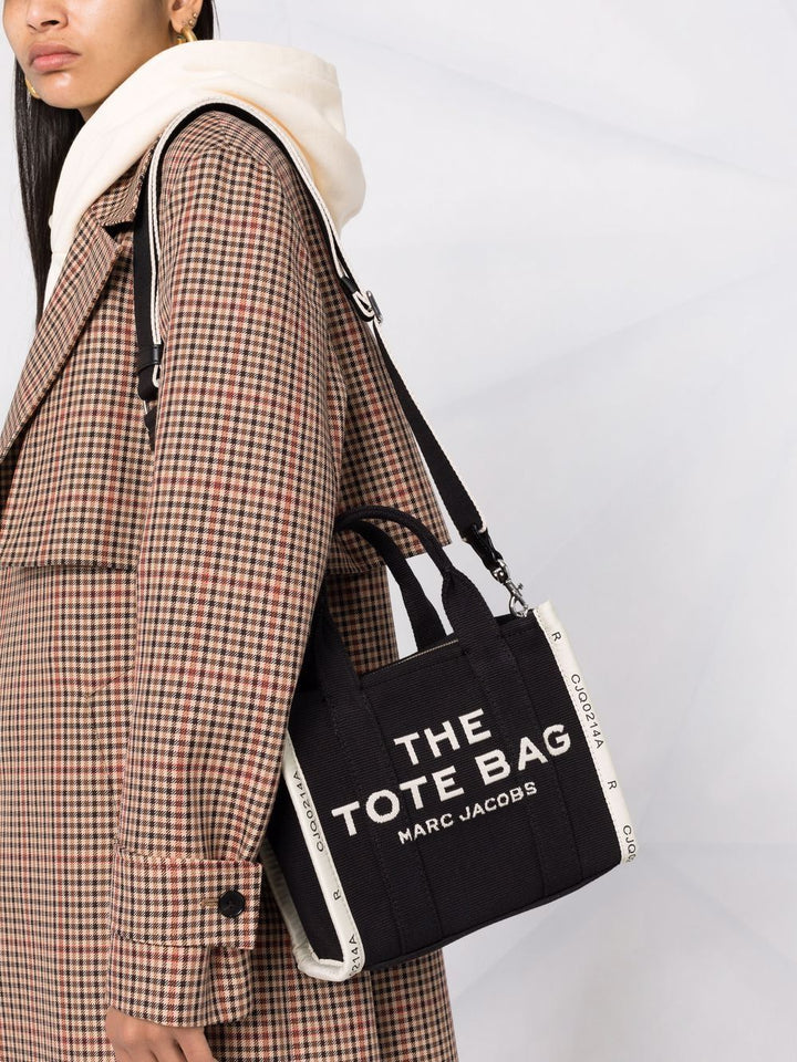 Person wearing a plaid coat holding a black tote bag with 'Marc Jacobs' branding.