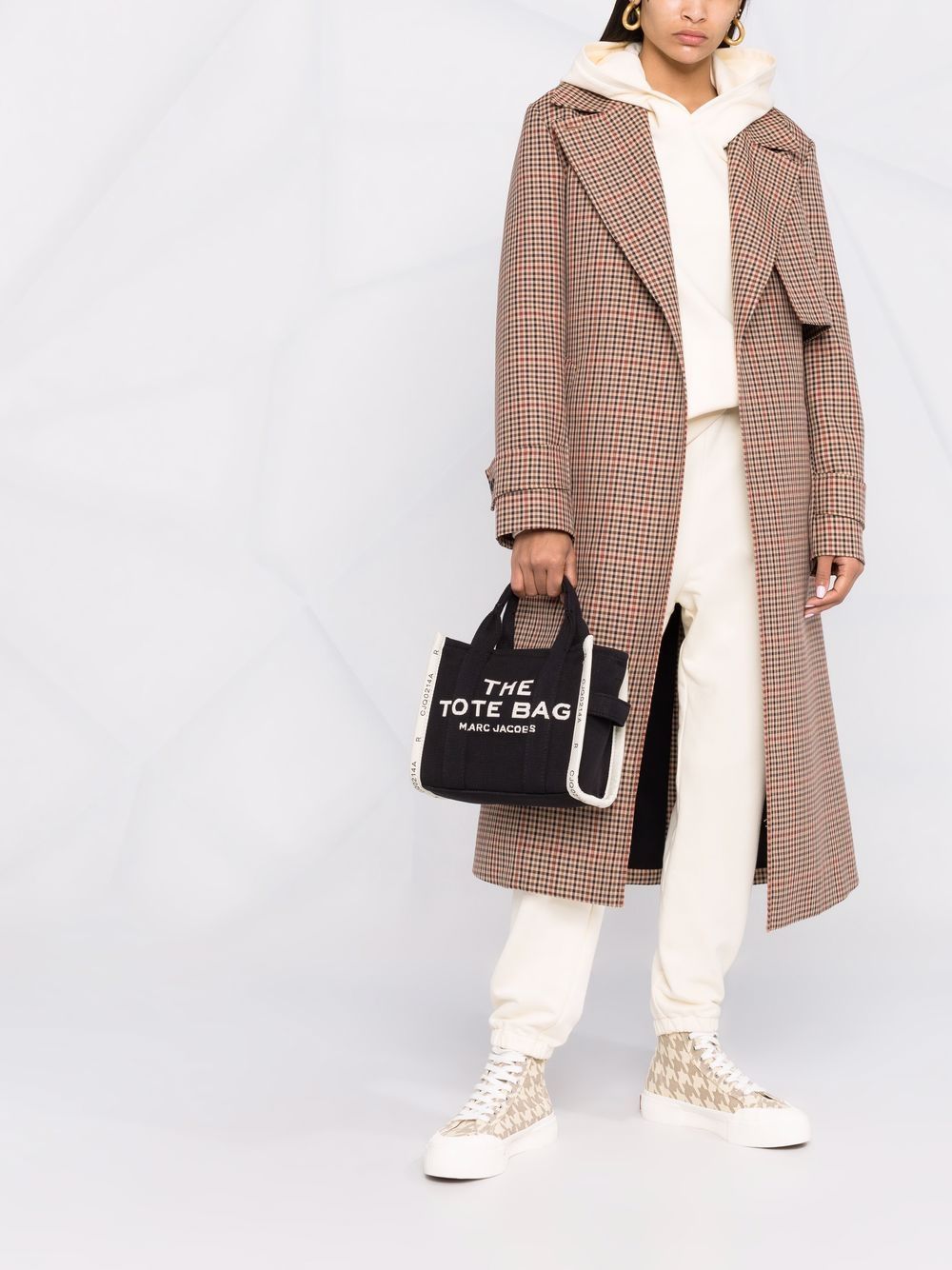 Person wearing a plaid coat holding a black handbag with 'The Tote Bag' text on a white background