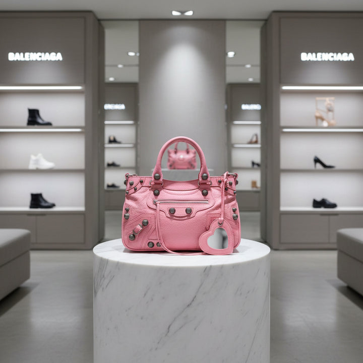 Pink handbag with black studs and a heart-shaped tag on a white background
